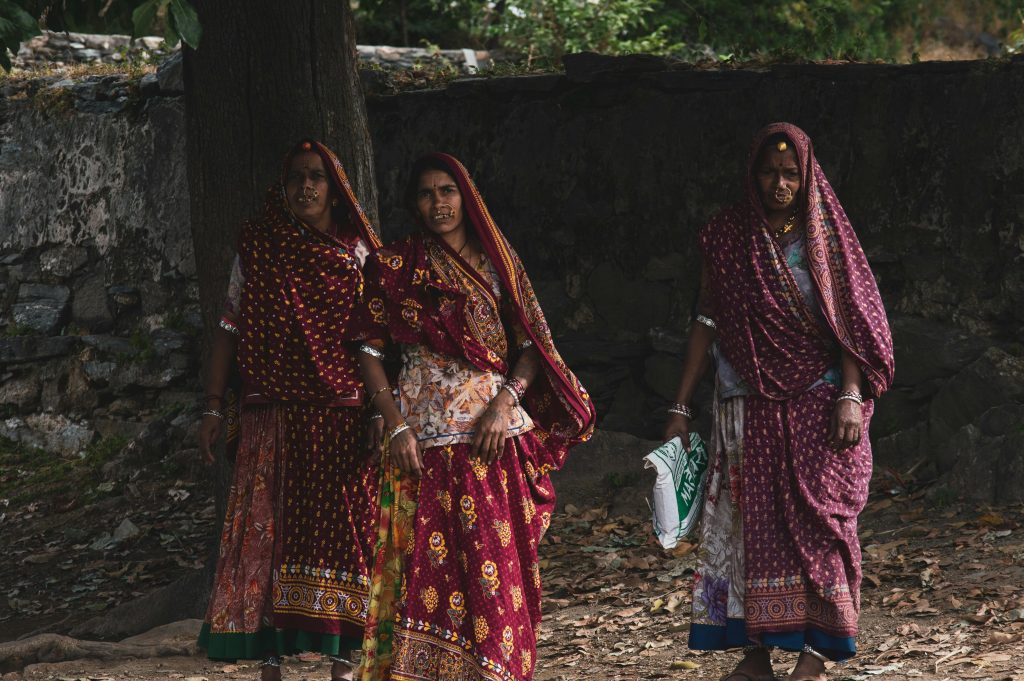 Three Indian women in vibrant sarees and jewelry, captured outdoors in Rajasthan, India.